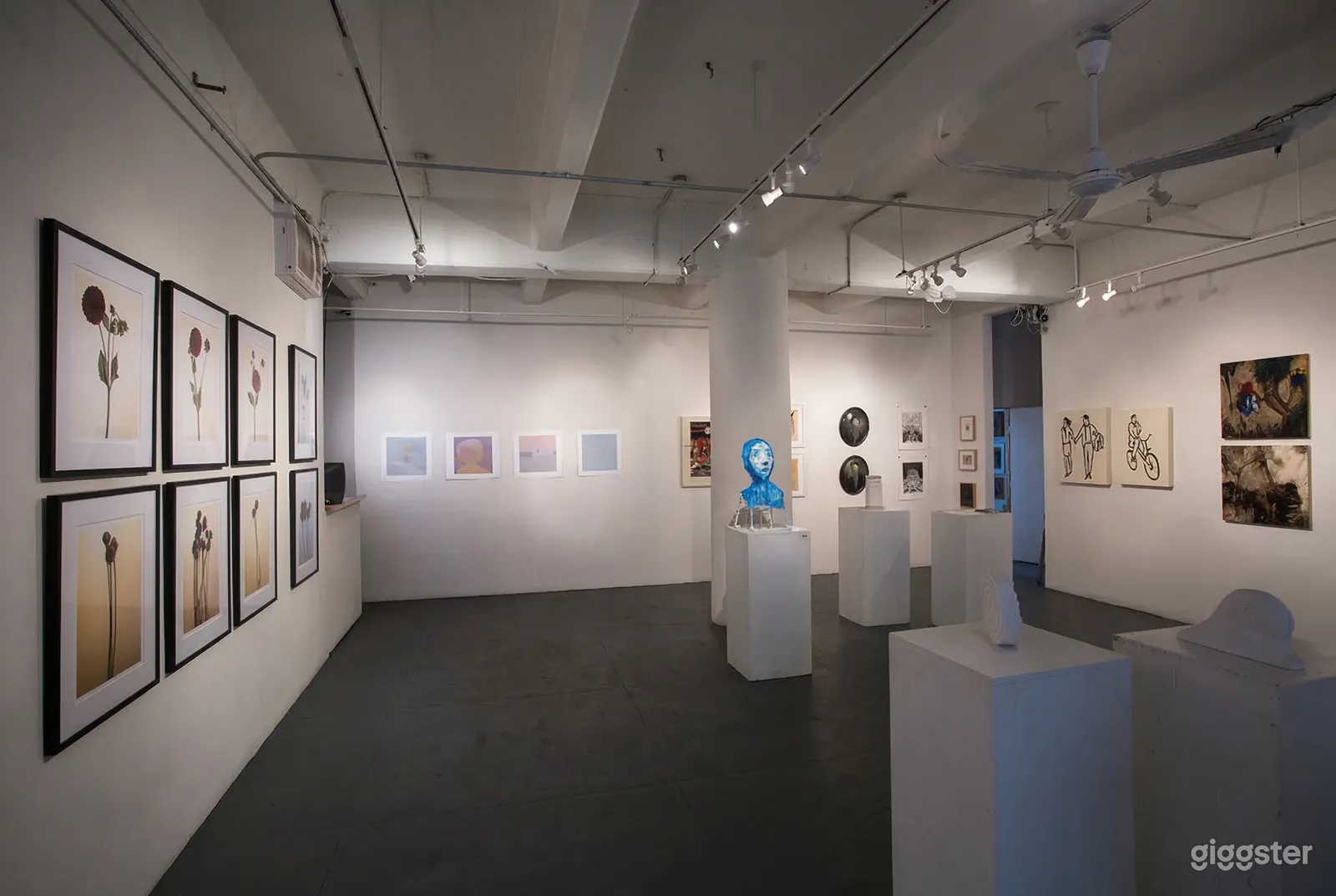 Various sizes and shapes of artwork are on the walls and sculptures are on stands in a gallery.