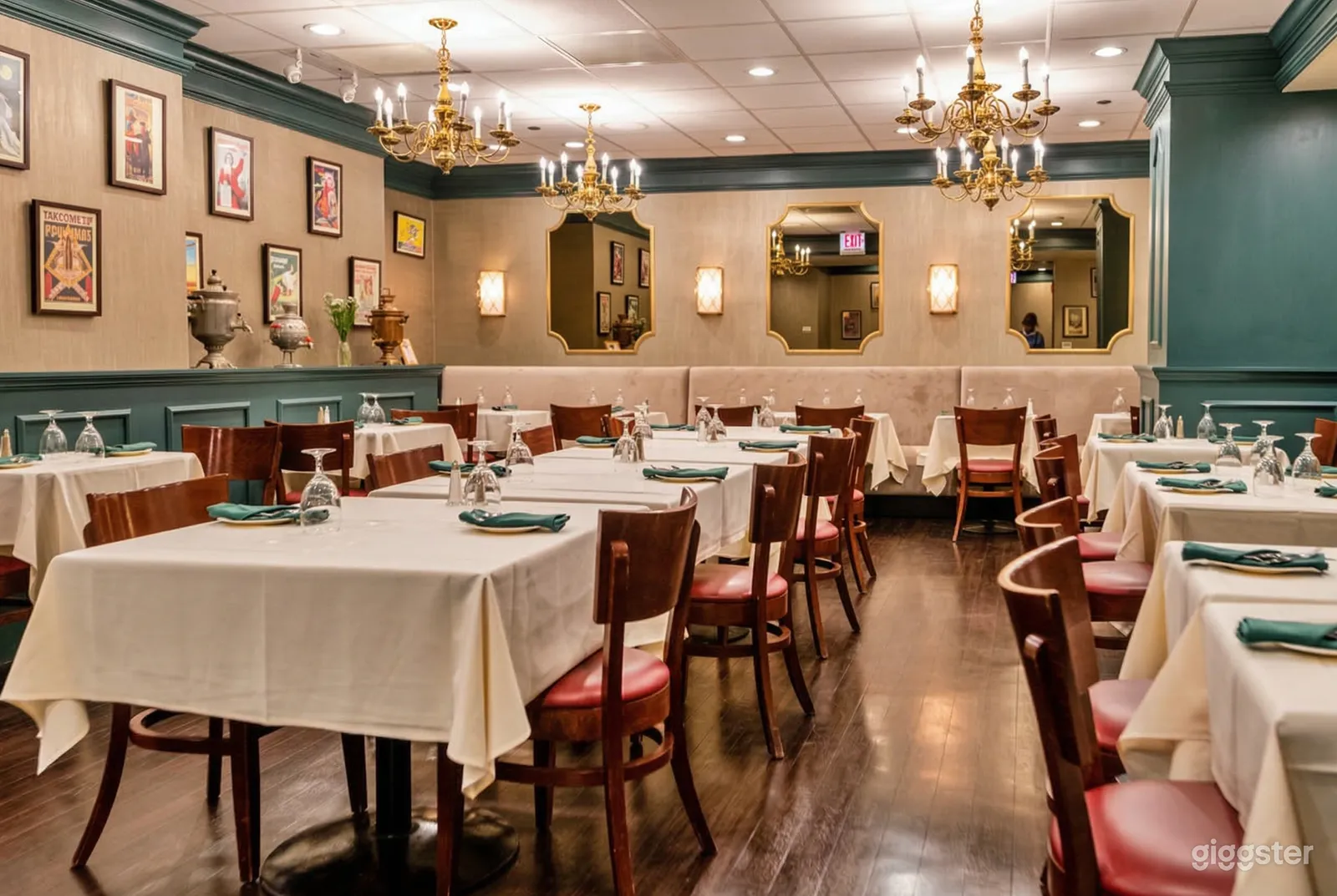 An event room is filled with multiple tables under traditional chandeliers with pictures and period vases along the wall.