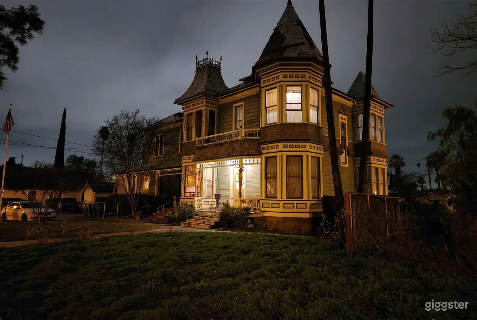 A Gothic-style mansion with a circular windowed front, is in darkness other than an upper room and the front porch.
