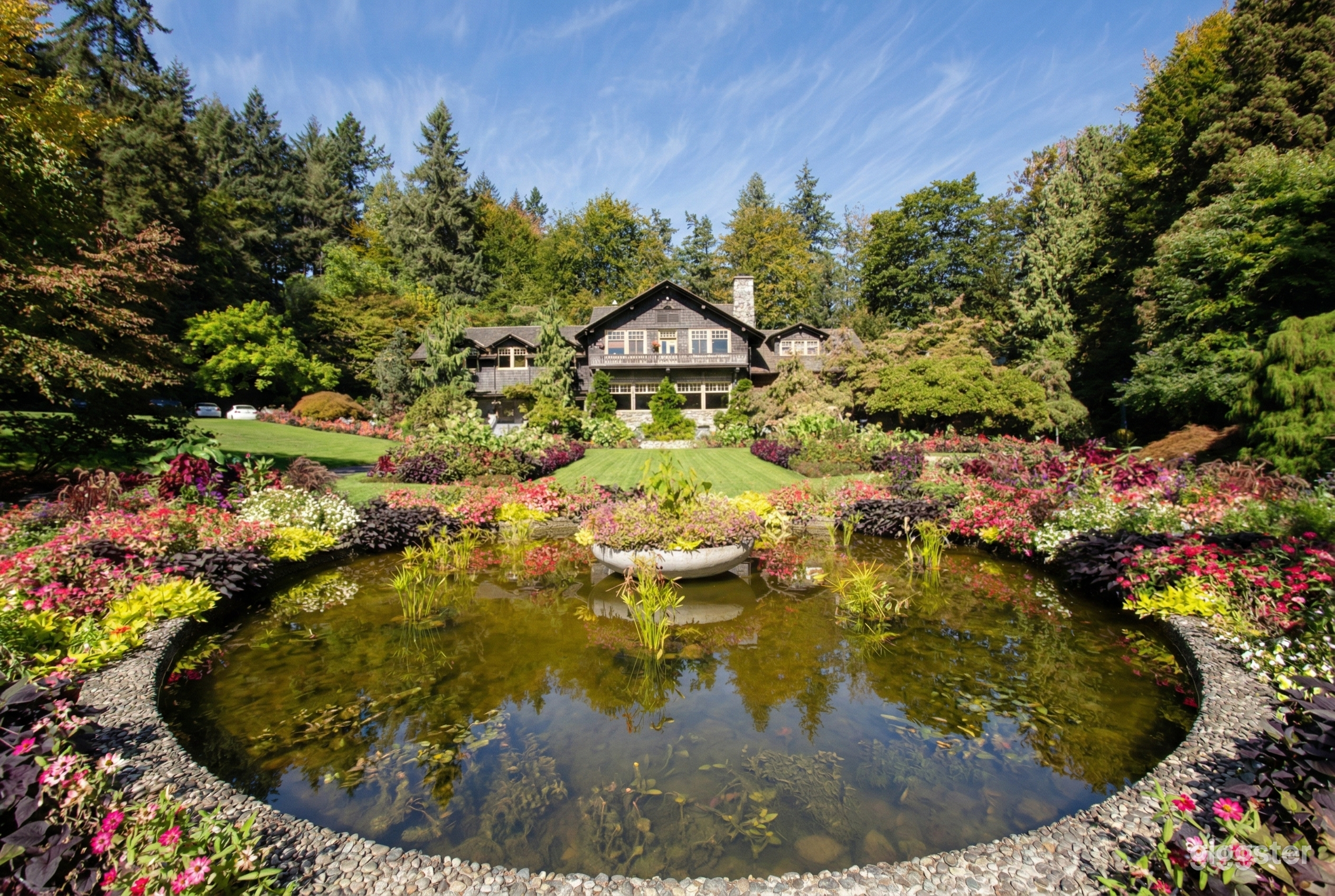 A chalet style home overlooks a grassy lawn and flower bordered pond.