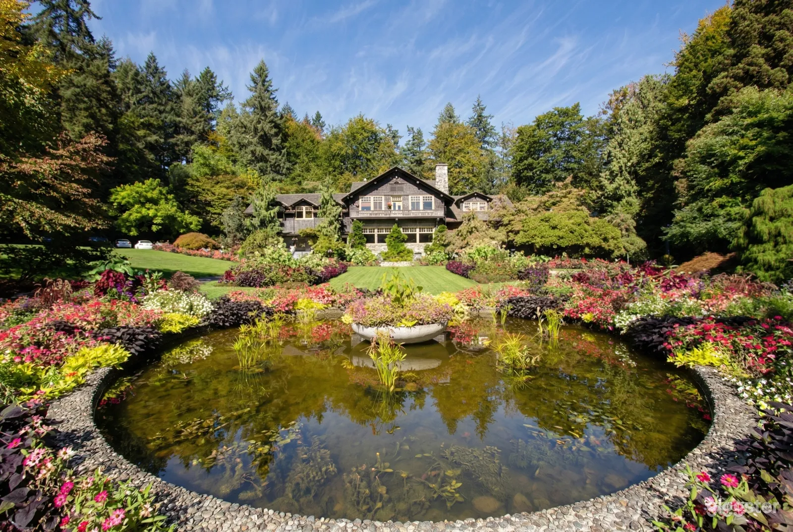 A chalet style home overlooks a grassy lawn and flower bordered pond.