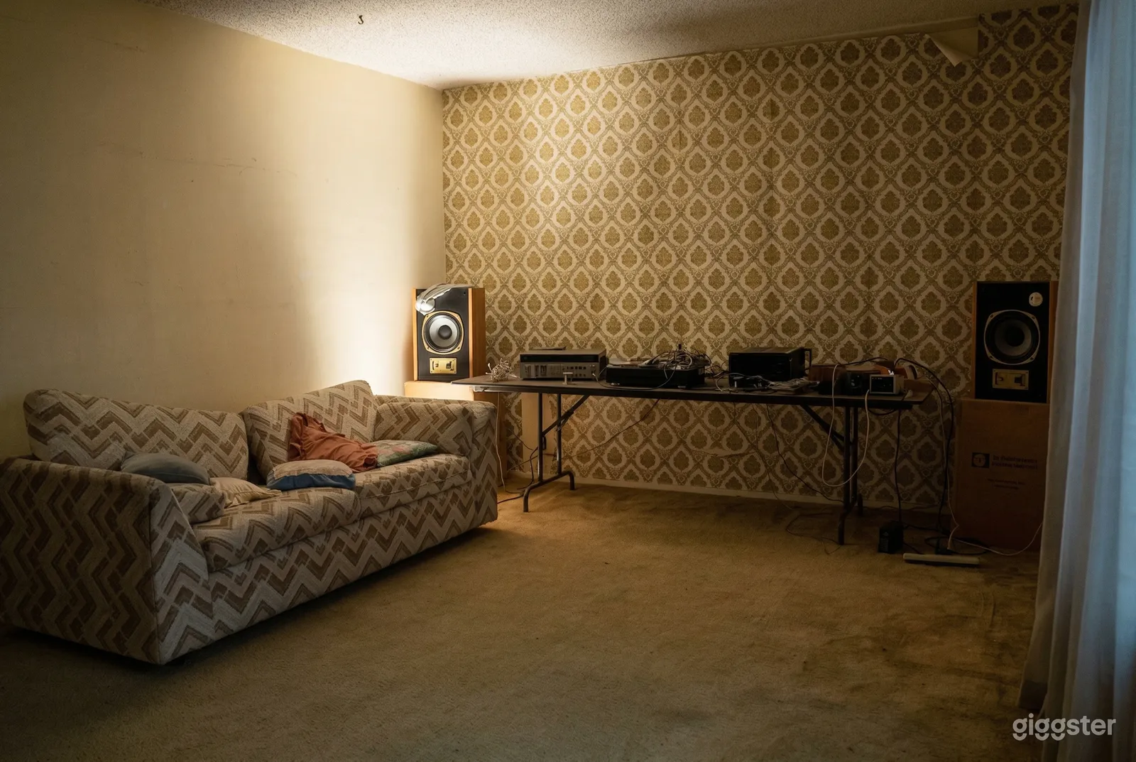 A vintage couch and stereo equipment sit in a dimly lit room with 70's wallpaper.