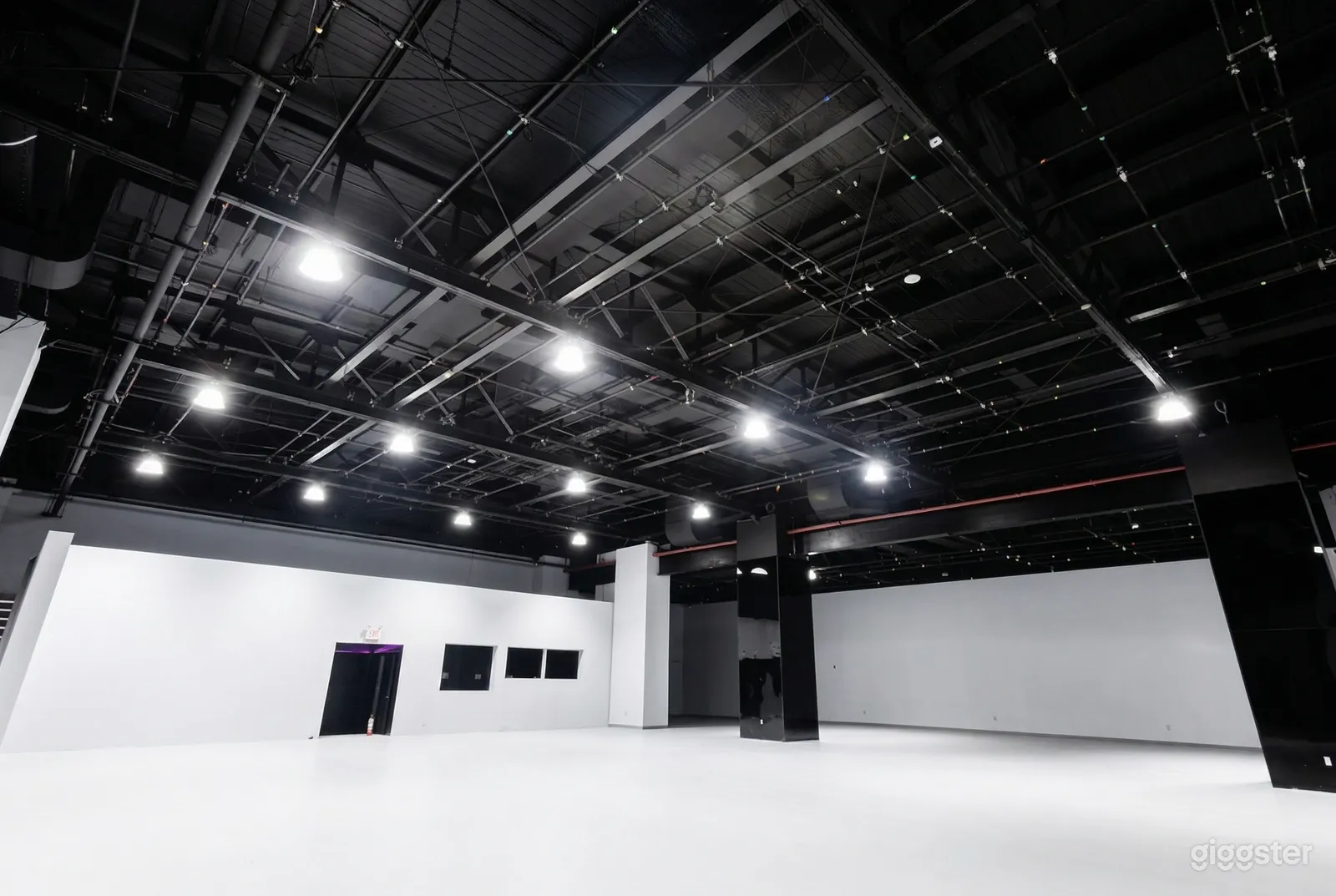 A large, empty warehouse with a glossy black ceiling and a white floor and walls.