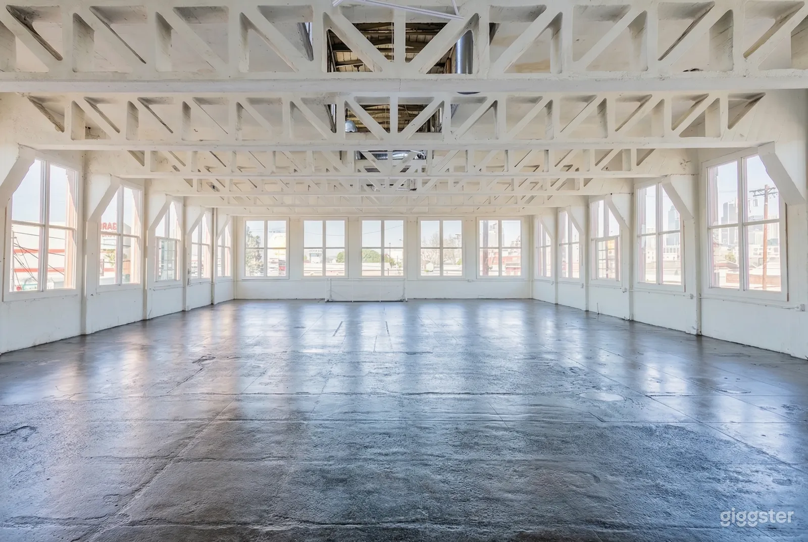 An expansive room with a metal beamed ceiling and large windows has a shiny cement floor.