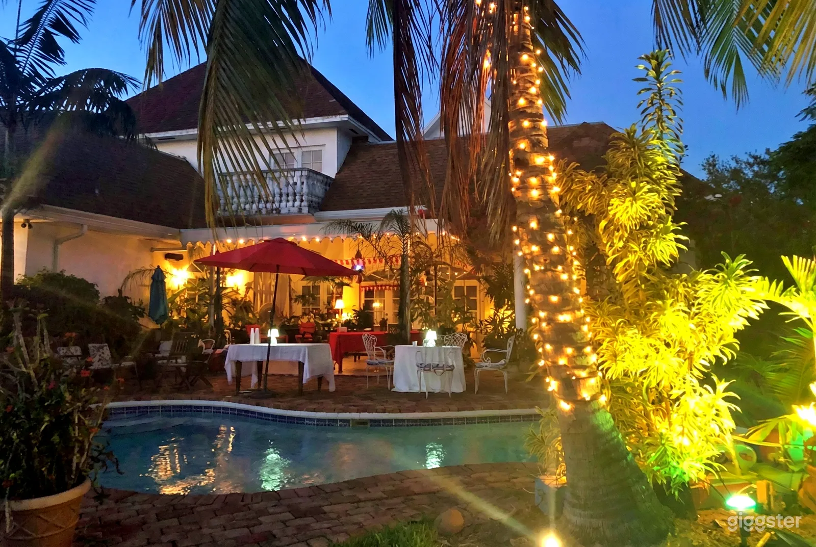 A softly lit poolside deck set up with tables and a red umbrella.