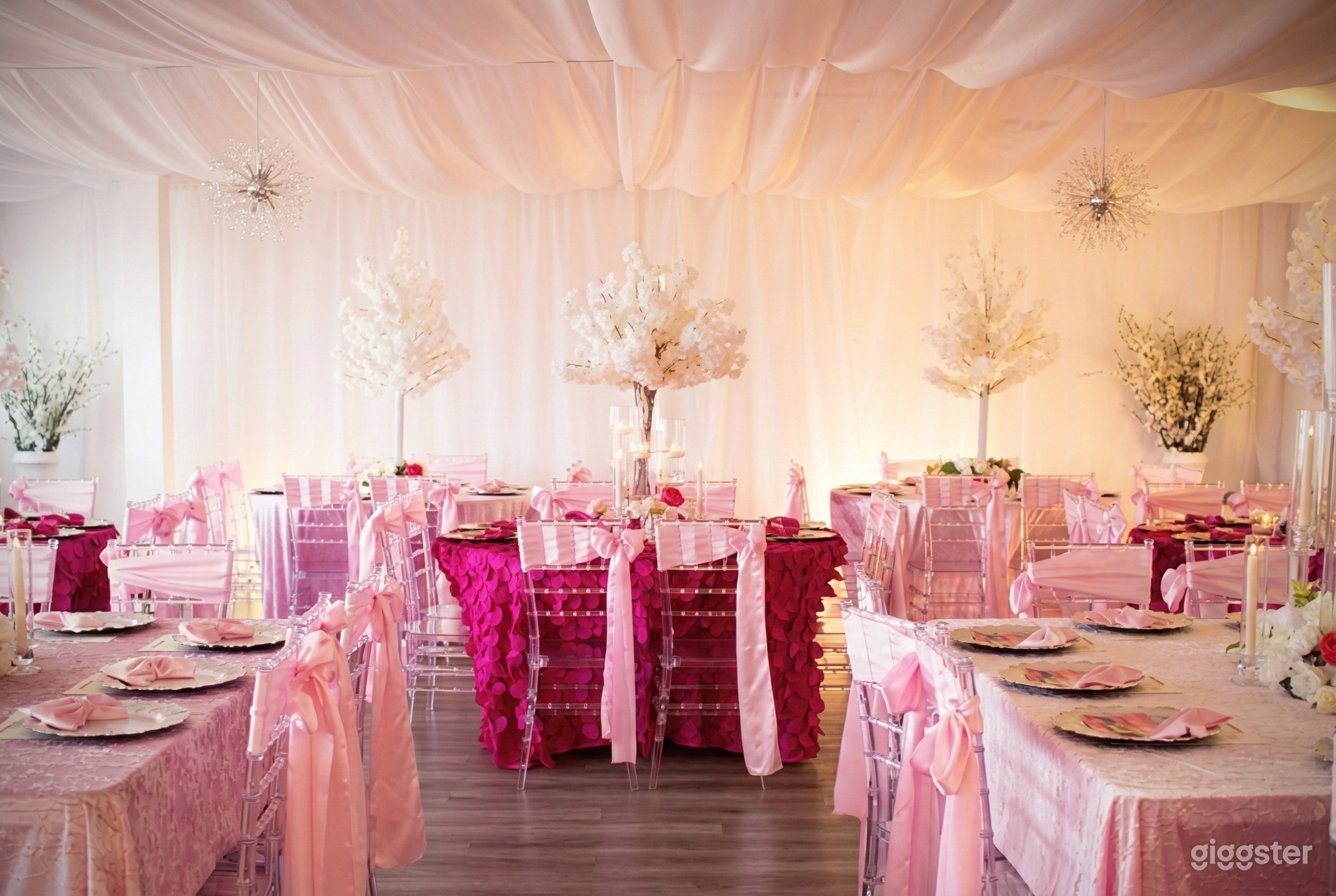 An event space with tables and chairs decorated in pink and white floral arrangements placed around the room.