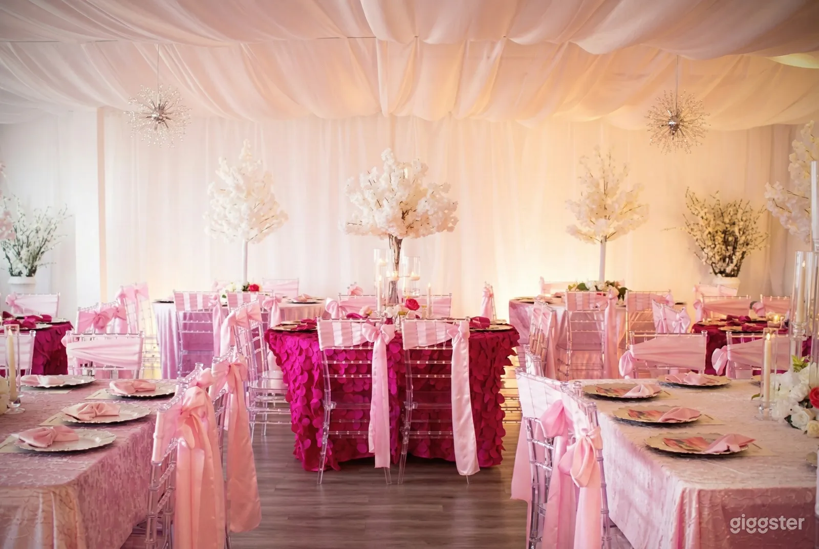 An event space with tables and chairs decorated in pink and white floral arrangements placed around the room.