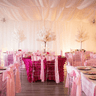 An event space with tables and chairs decorated in pink and white floral arrangements placed around the room.