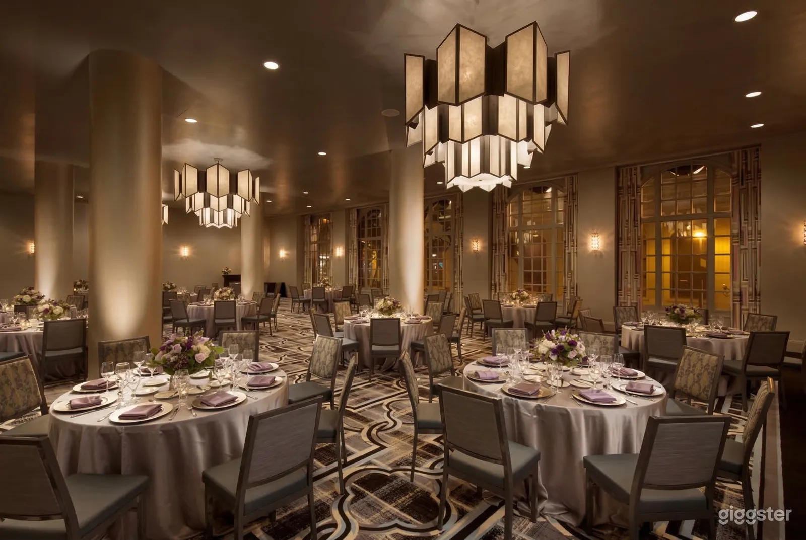 Round tables with multiple place settings in a ballroom-style room with modern chandeliers overhead.